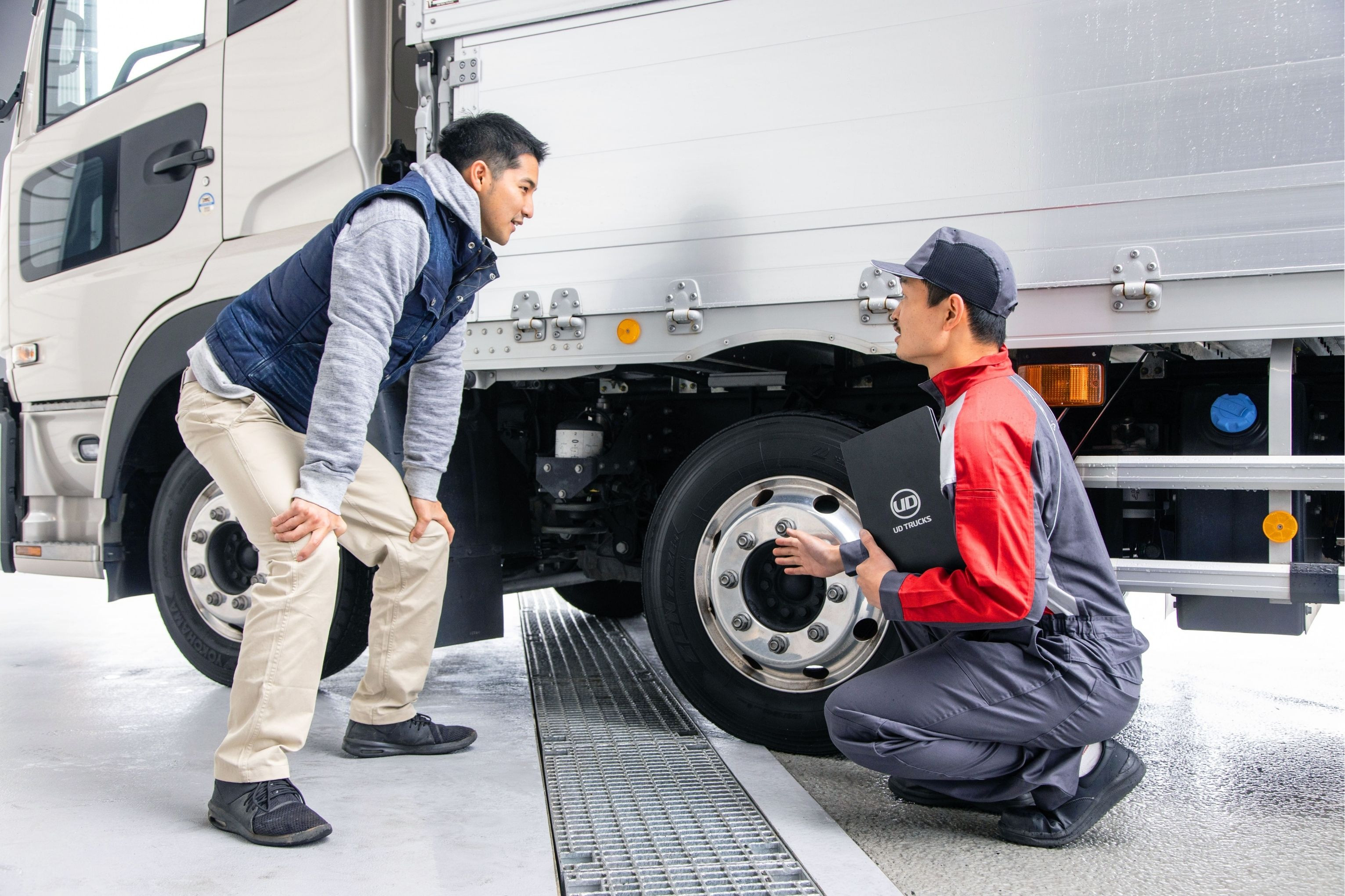 トラックのタイヤを点検する整備士と話す男性