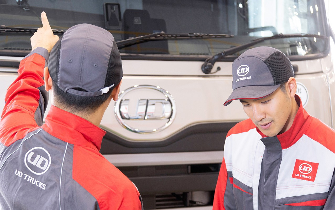 Two mechanics in red uniforms inspect a large white truck.