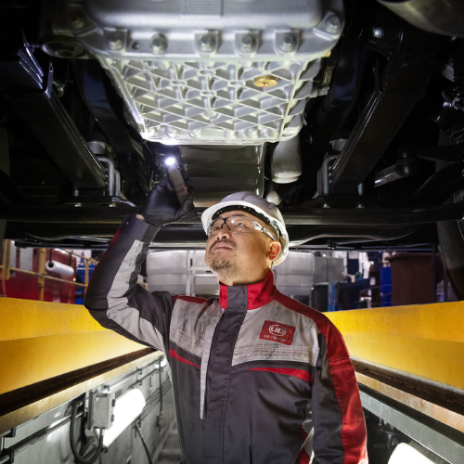 Mechanic inspects undercarriage of a vehicle with a flashlight in a workshop.