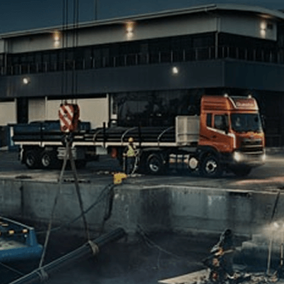 Lori oren di tapak pembinaan berhampiran bangunan dua tingkat pada waktu malam.