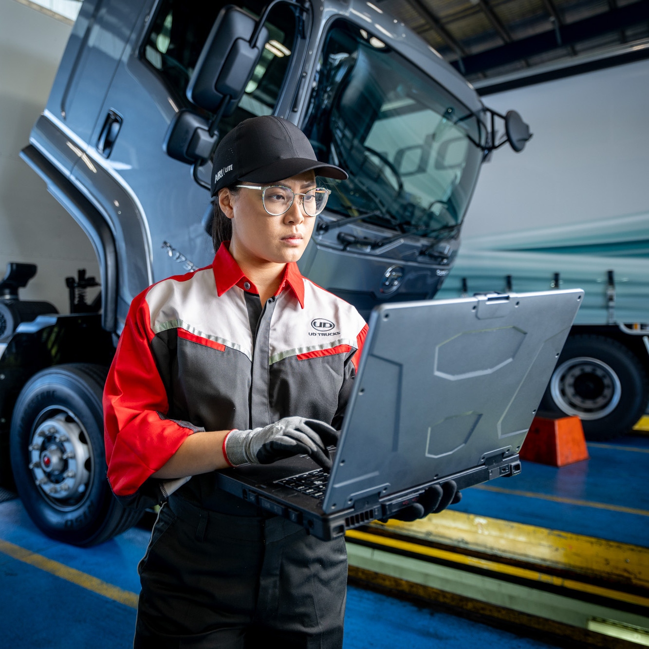 Mechanic with safety gear using a laptop in front of a large truck in a garage.
