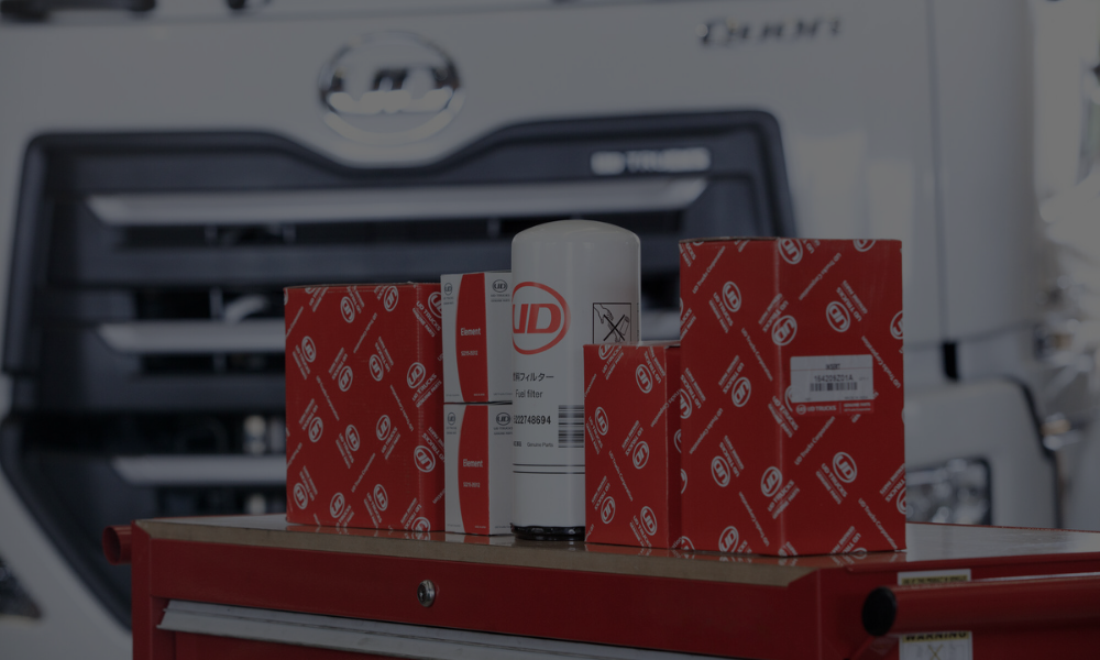 Truck parts and filter cartridges on a red toolbox, blurred truck grill in background.