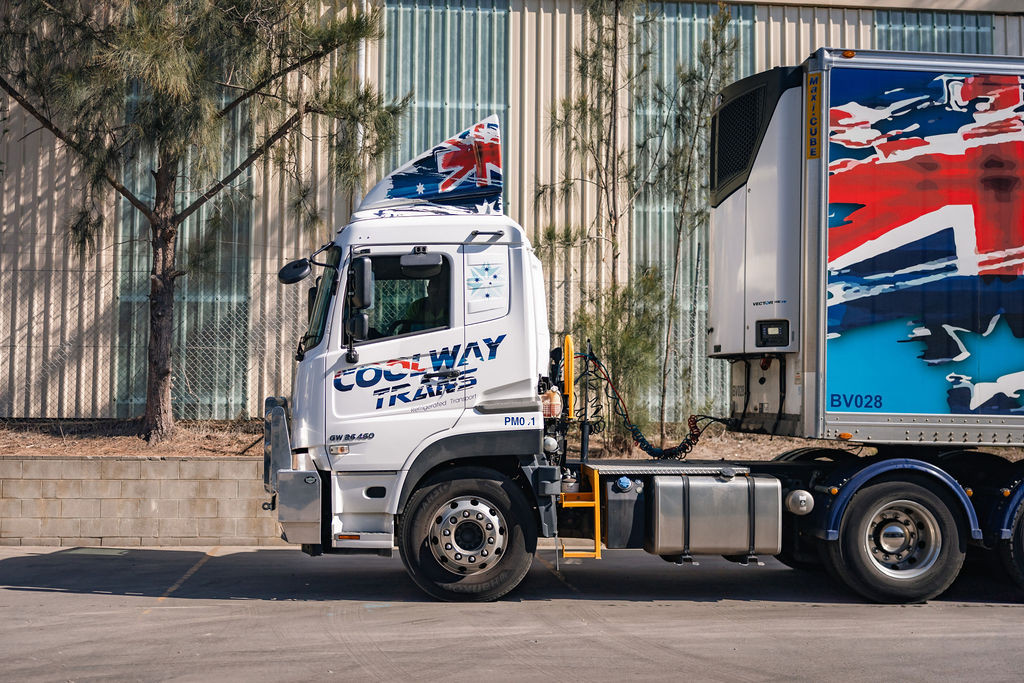 White truck with Australian flag design parked beside a corrugated metal building.