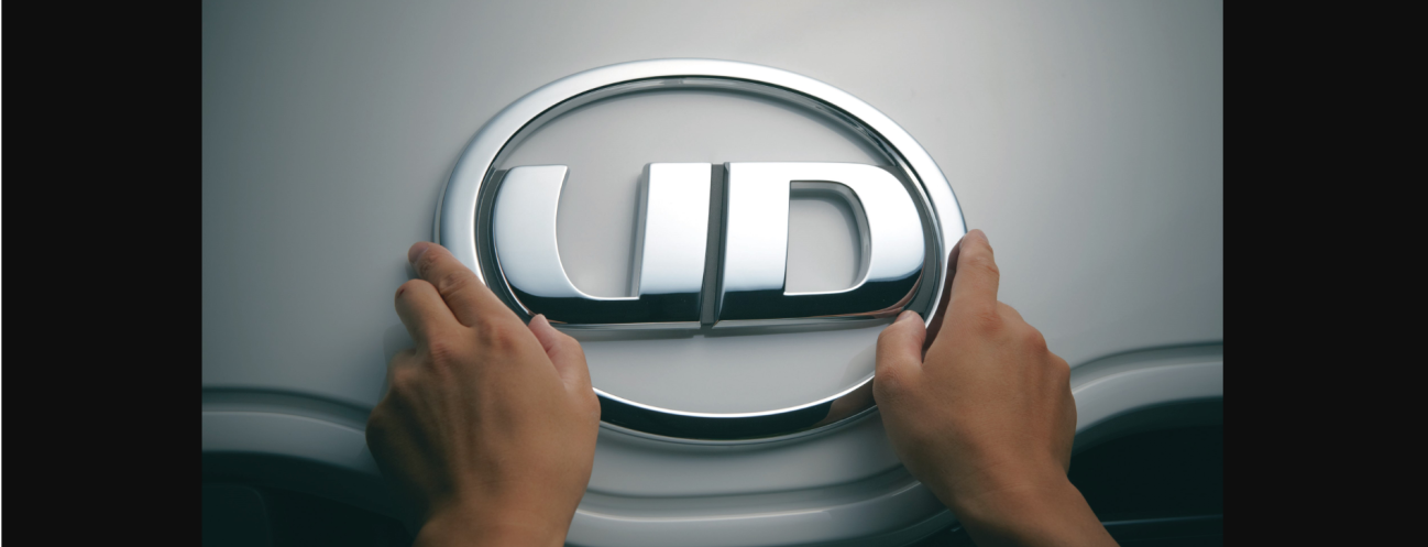 両手でUDロゴエンブレムを触っているシルバーの車ボンネット