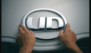 両手が車のUDロゴエンブレムを触れている