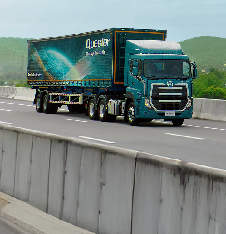 รถบรรทุกเทรลเลอร์สีเขียววิ่งบนทางด่วน มีภูเขาอยู่ด้านหลัง