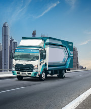 شاحنة زرقاء تسير على جسر مع أبراج المدينة في الخلفية وسماء صافية